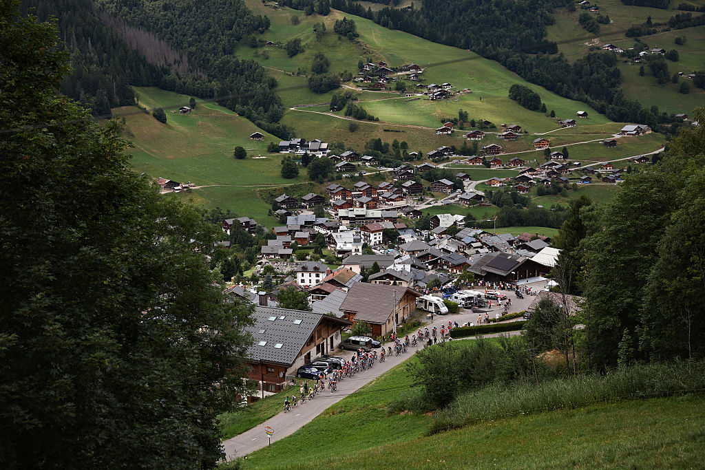 The pack of riders (peloton) cycles past the village of Areches in the ascent of Col du Pre during the 19th stage of the 112th edition of the Tour de France cycling race, 93.1 km between Albertville and La Plagne, in the French Alps, on July 25, 2025. The 19th stage of the Tour de France was shorted from its initial 129.9 km route, bypassing the Col des Saisies where an outbreak of nodular dermatitis in a herd of cattle was discovered, prompting organizers to modify the race route. (Photo by Anne-Christine POUJOULAT / AFP)