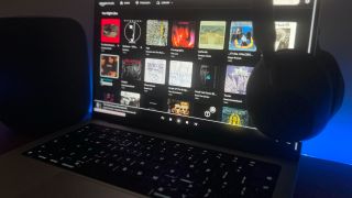 A photograph of a laptop playing Amazon Music Unlimited, with a pair of Sony speakers draped over the right-hand side. On the left is a Sonos speaker.