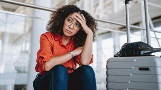 Woman sitting on the floor of the airport next to suitcase