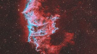 A swirling red nebula is pictured against a distant starfield