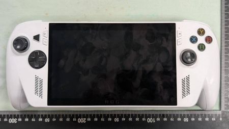 White Xbox handheld sitting on light green surface next to ruler.