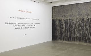 A gallery with 2 featured walls. The wall on the left is white with text on it and the one on the right is a grey and black abstract painting
