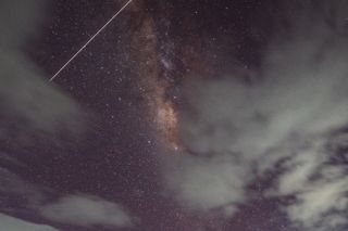 a streak of white light passes in front of stars in the night sky