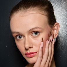 girl with blue eyes who has her hand and almond manicure resting on her face