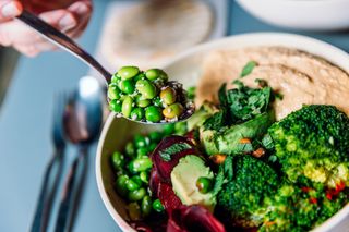 Bowl of healthy dinner comprising of salad, hummus and vegetables with avocado and spinach