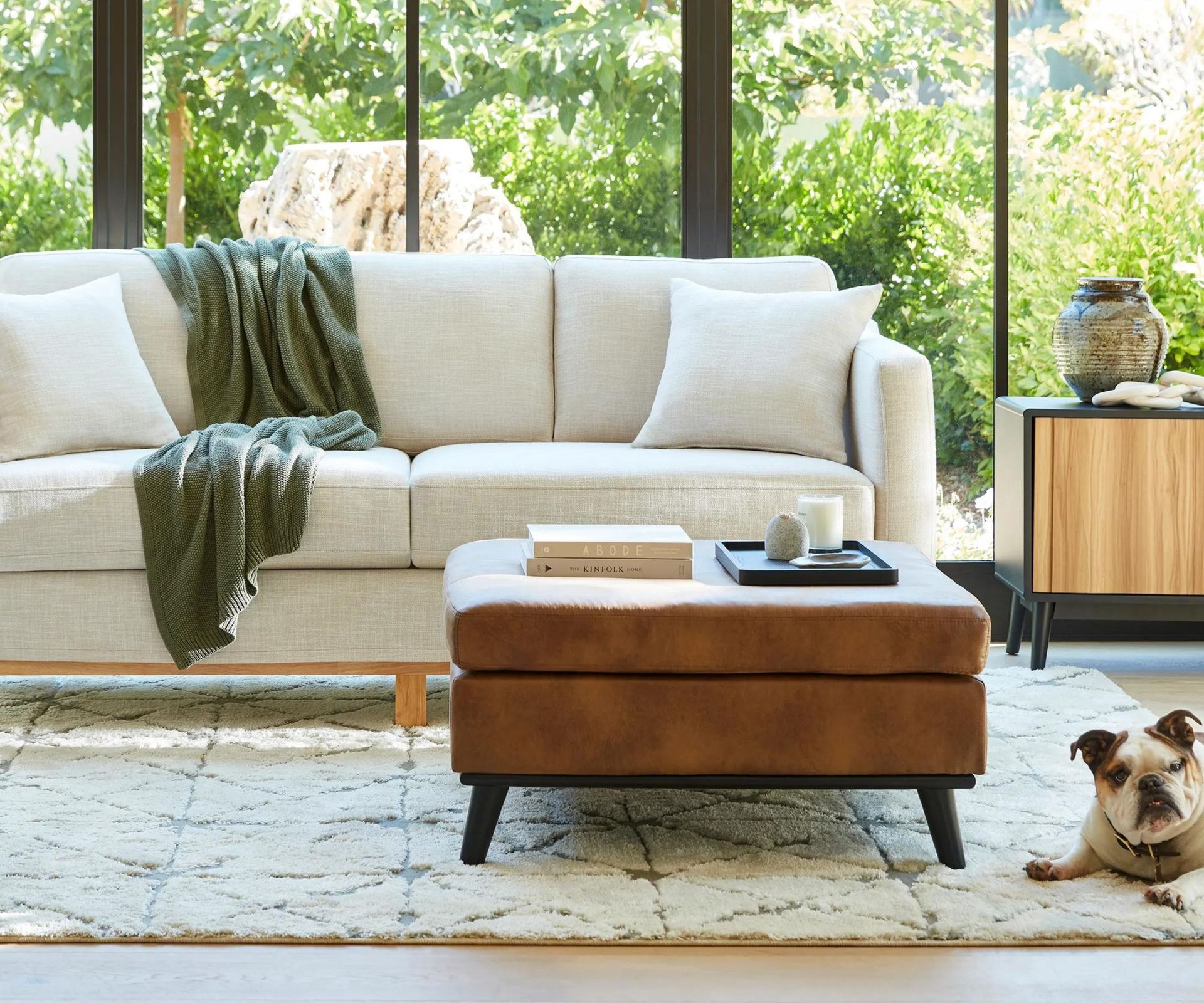 White sofa with footstool against a window with a garden view.
