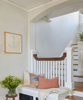 Entrance area with neutral walls, colorful cushions on the bench and a flower vase