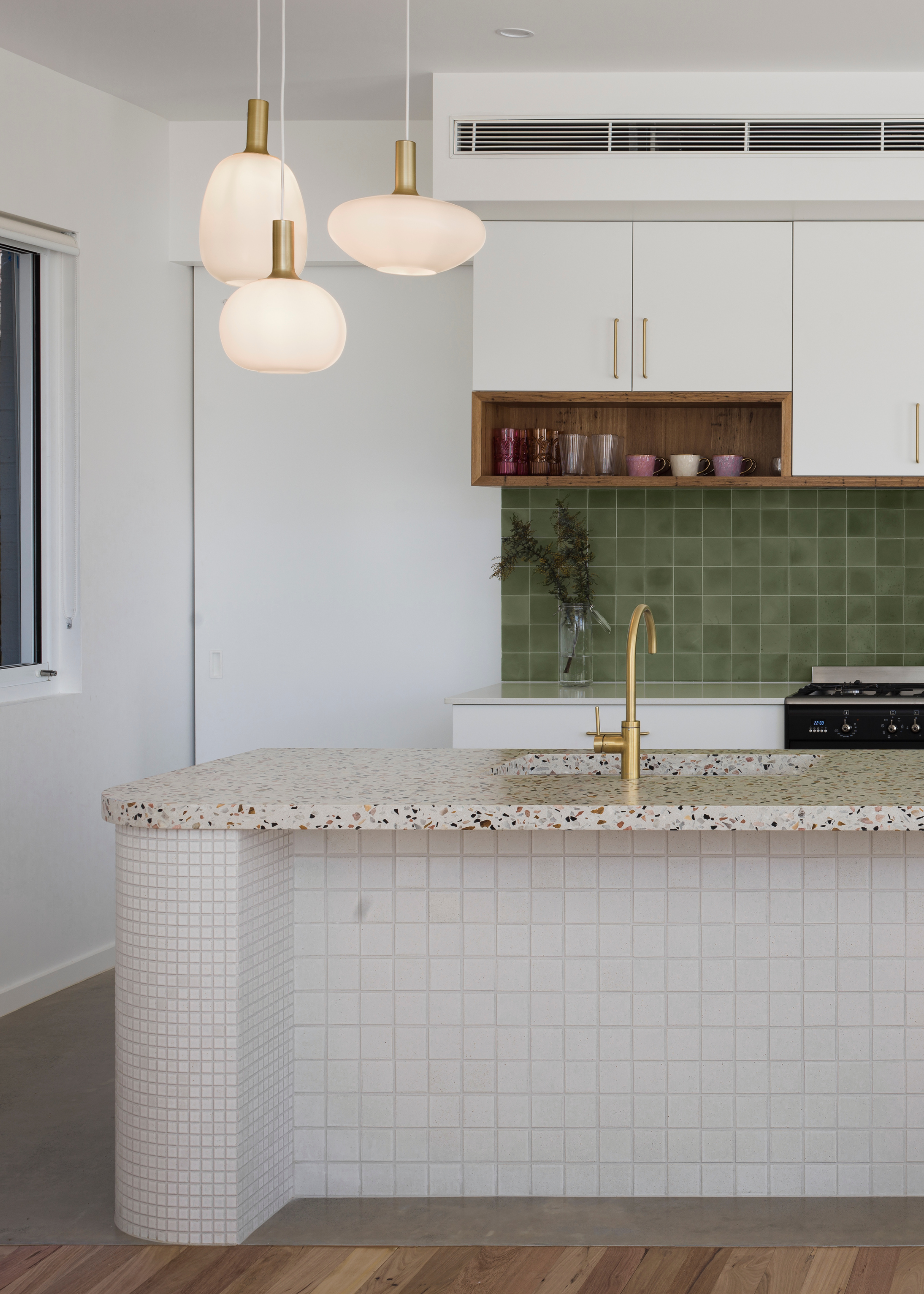 A small kitchen with a terrazzo island, a tiled backsplash and a trio of ceiling lights