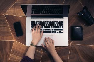 Hands typing on laptop computer on patterned wooden surface