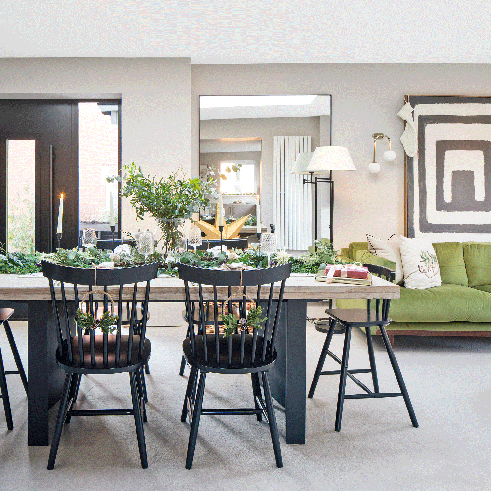 a large open plan dining living area with a dining table with black chairs set for Christmas and a green chaise sofa