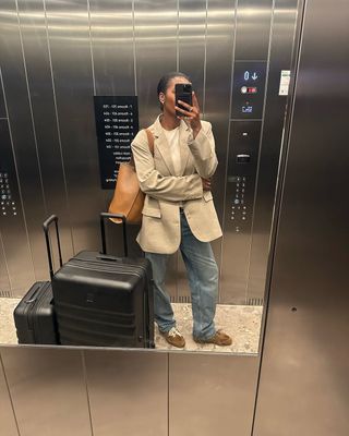 Marilyn in a beige blazer, suede trainers and jeans with suitcases