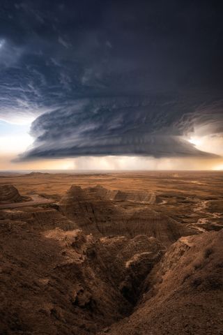 Dramatic supercell storm over an expansive, rugged canyon landscape at sunset