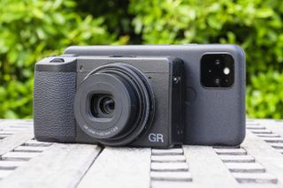 A Ricoh GR III X camera in front of a phone