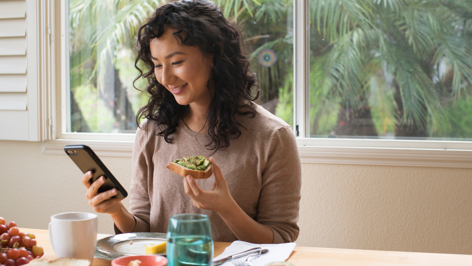 woman eating avocado on toast while looking at her phone