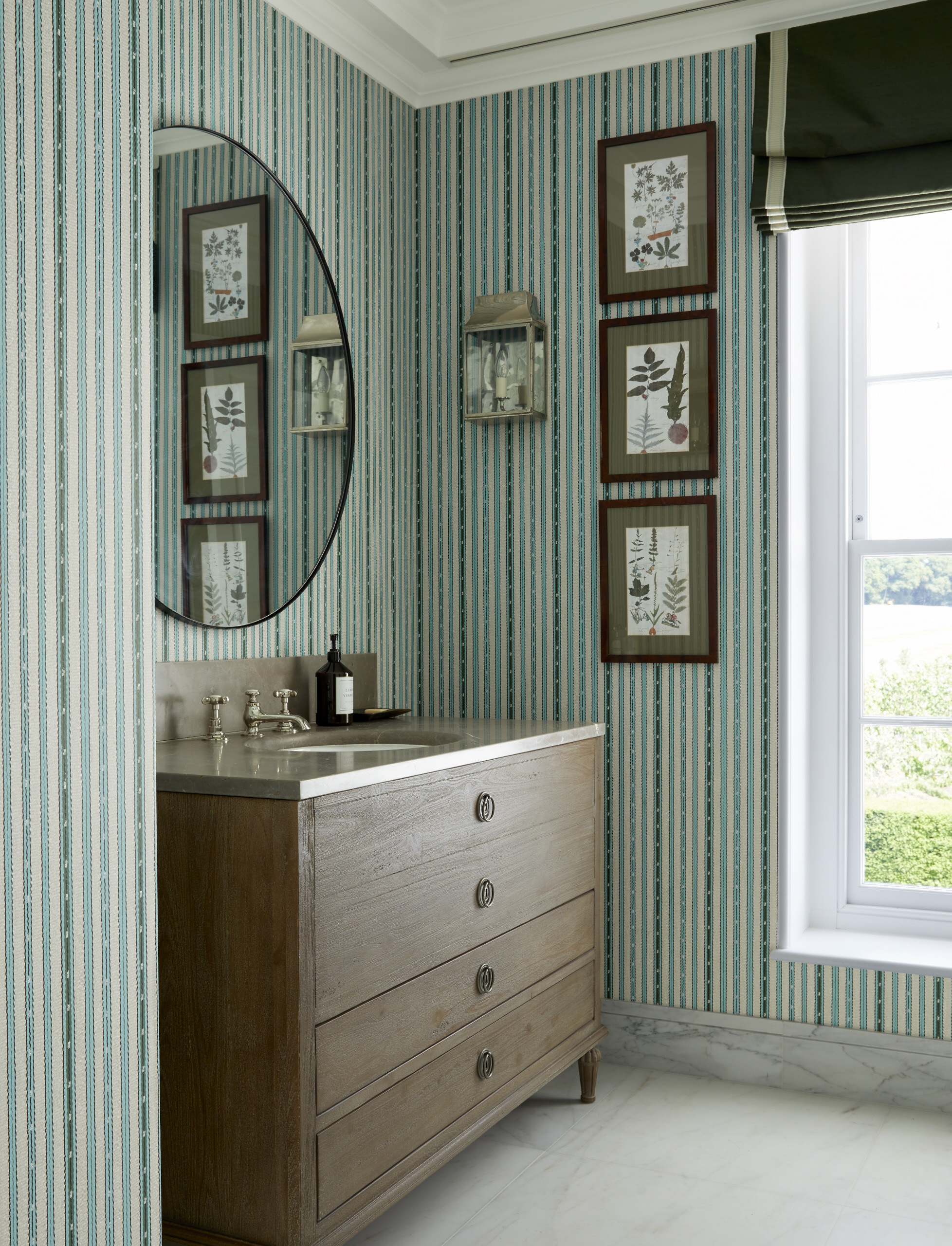 A bathroom with green striped wallpaper, a wooden vanity, and a trio of botanical prints on the wall