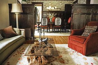 A mission style living room with a wooden craftsman style partition, a red accent chair, and a glass coffee table