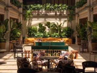 The leafy inner courtyard of a hotel features plenty of vegetation and Art Deco as well as modern rustic furniture.