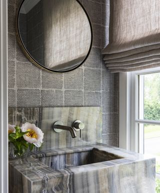 A powder room with grey marble sink and grey wallpapered walls