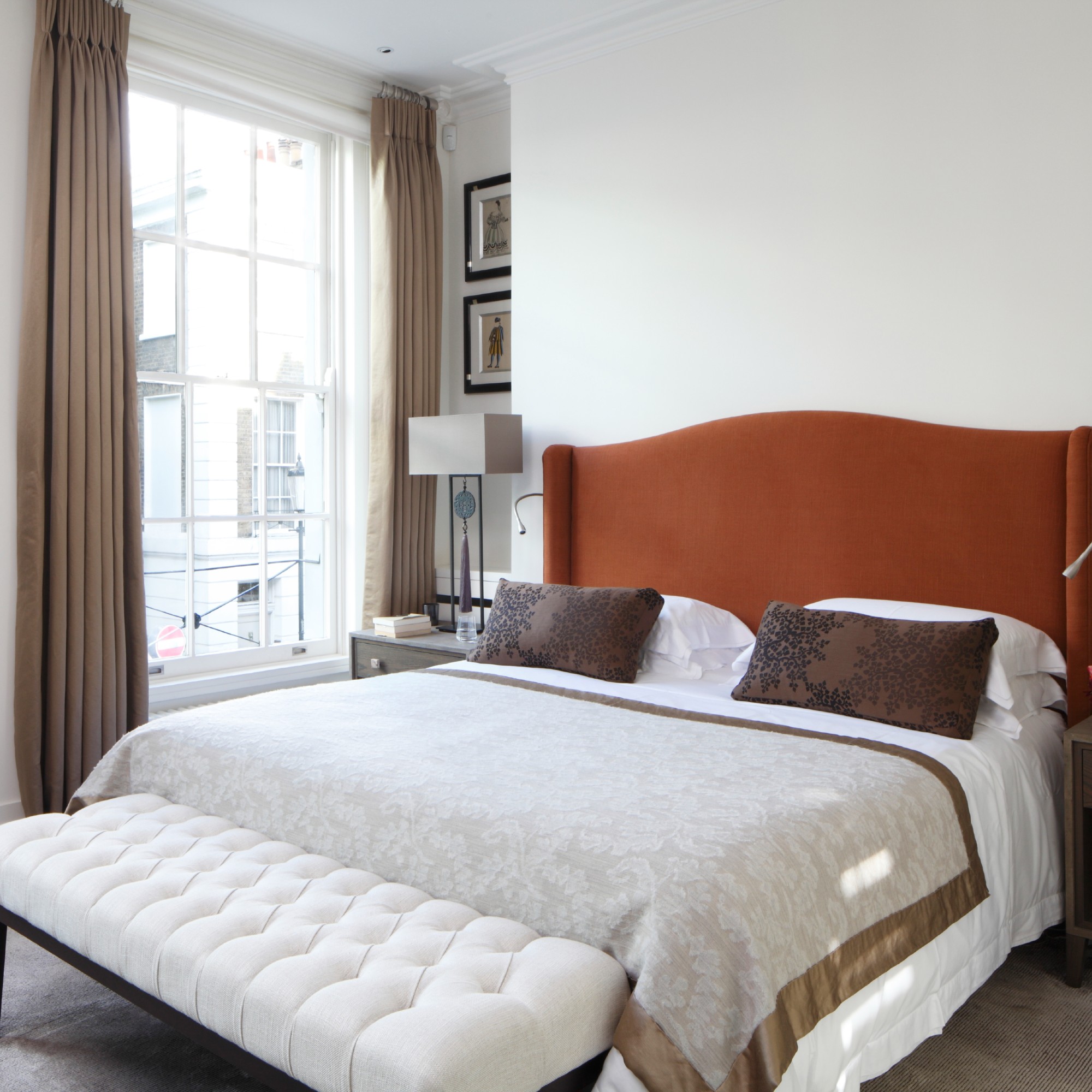 A white bedroom with an upholstered statement headboard in a rusty shade and brown pleated curtains