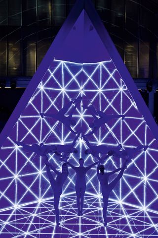 A group of gymnast creating a giant kaleidoscope with a giant lit up triangle display in the background