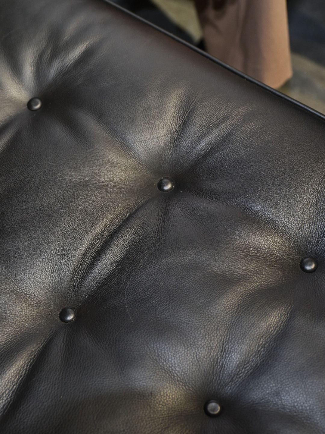 Close-up of the Heal&rsquo;s Hepburn sofa&rsquo;s coated black leather, showing light scratches and natural wear across its buttoned seat.