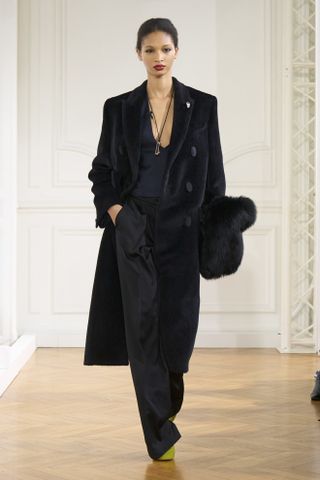 Model Givechy mengenakan jas hitam, celana hitam, atasan berpotongan rendah, dan kalung panjang