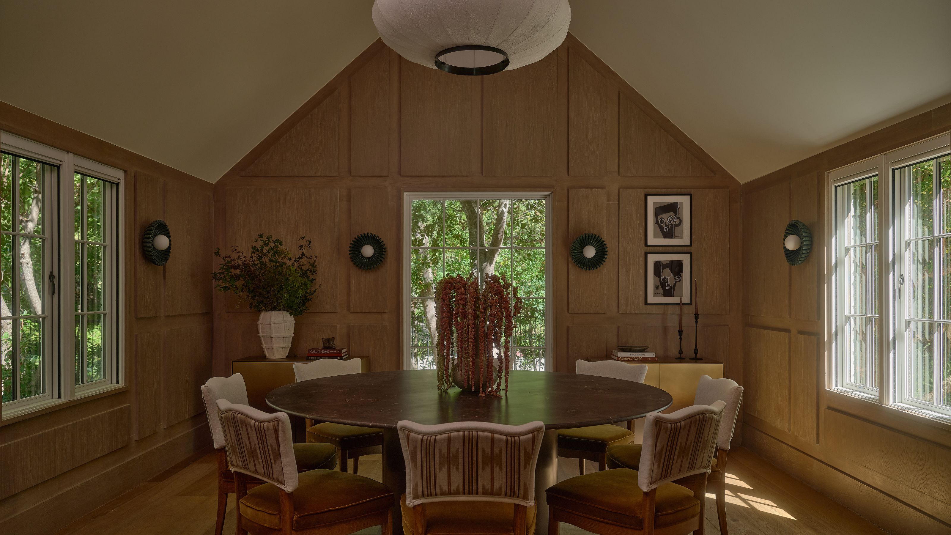 a wooden clad dning room with paneled walls and a vaulted ceiling with a large round table
