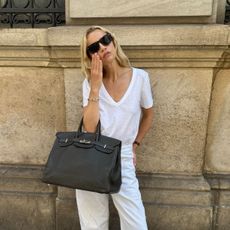A woman wearing a white t-shirt, white jeans, and a black leather bag