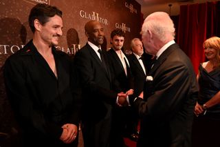 Denzel Washington wears a black suit as he meets King Charles, who is wearing a tuxedo, at the London premiere of Gladiator II