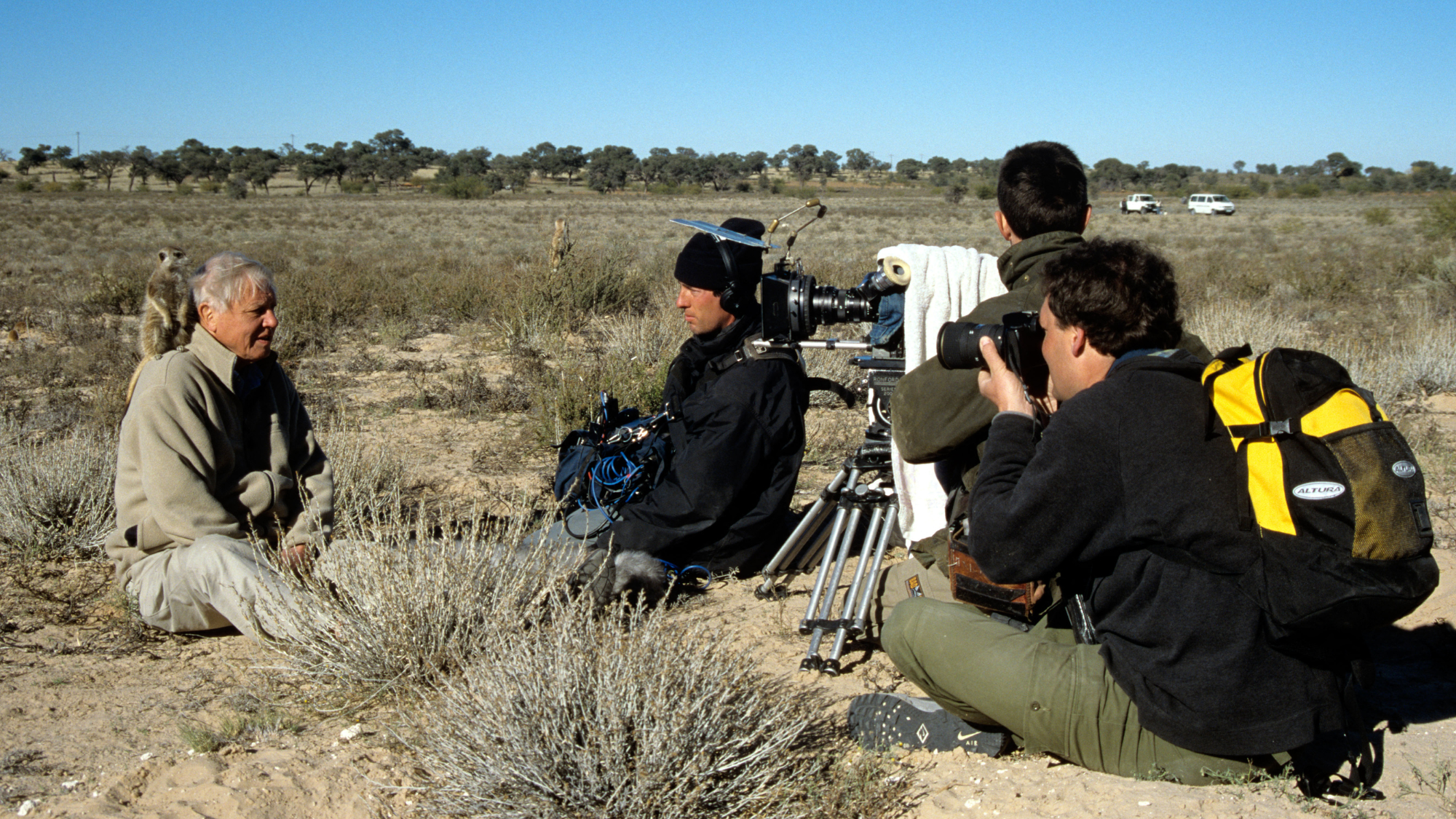 David Attenborough with a meerkat on his shoulder during filming