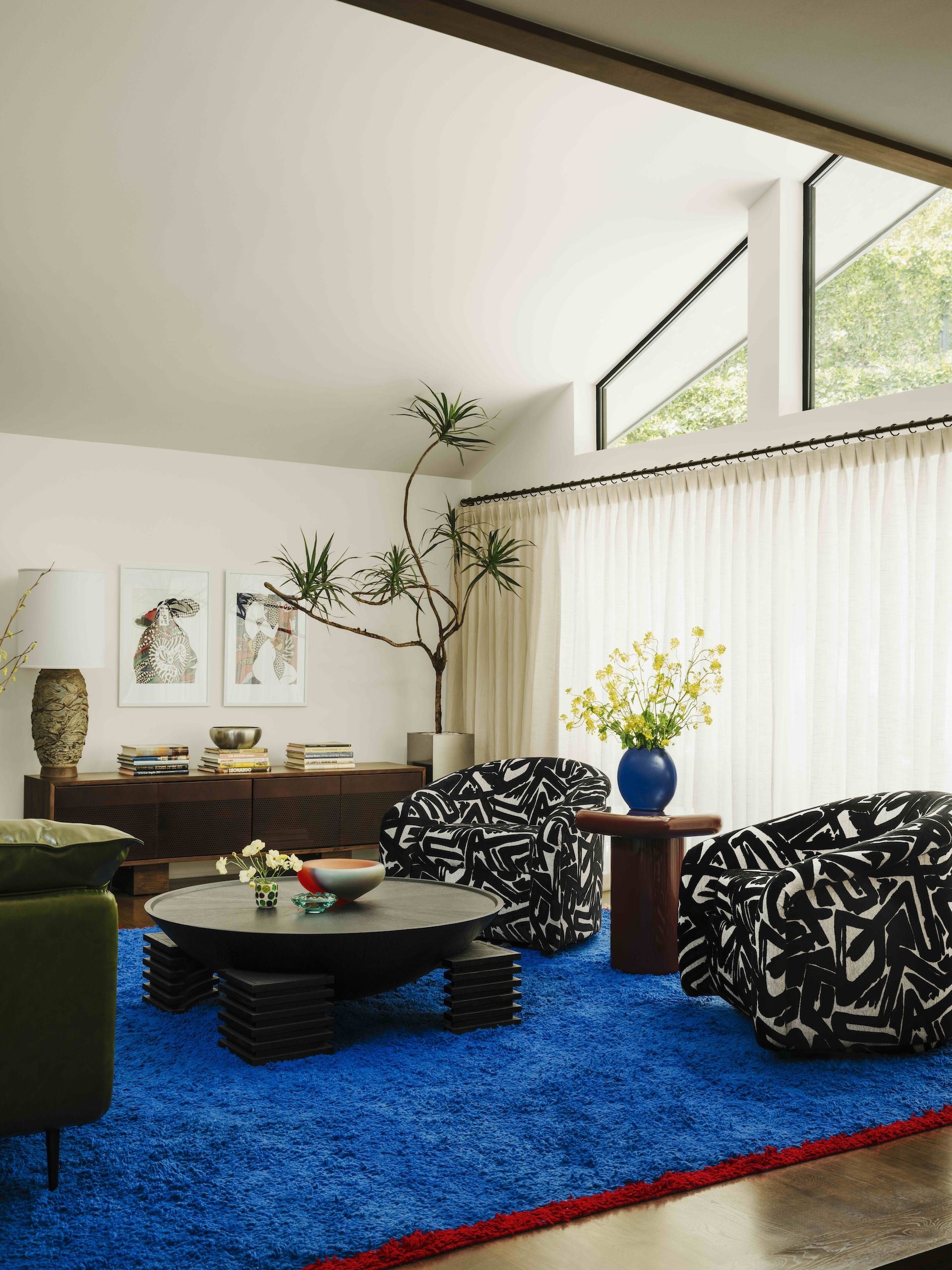 A contemporary living room with bright blue rug, graphic upholstered chairs and sculptural coffee table