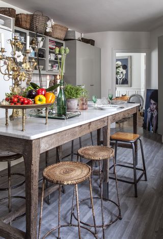 An industrial style kitchen with a freestanding rustic wooden and marble kitchen island with wooden stools with metal legs and rattan baskets around the kitchen