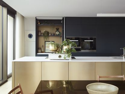A modern kitchen with gold gloss kitchen cabinets on a kitchen island, and dark navy cabinets on the walls