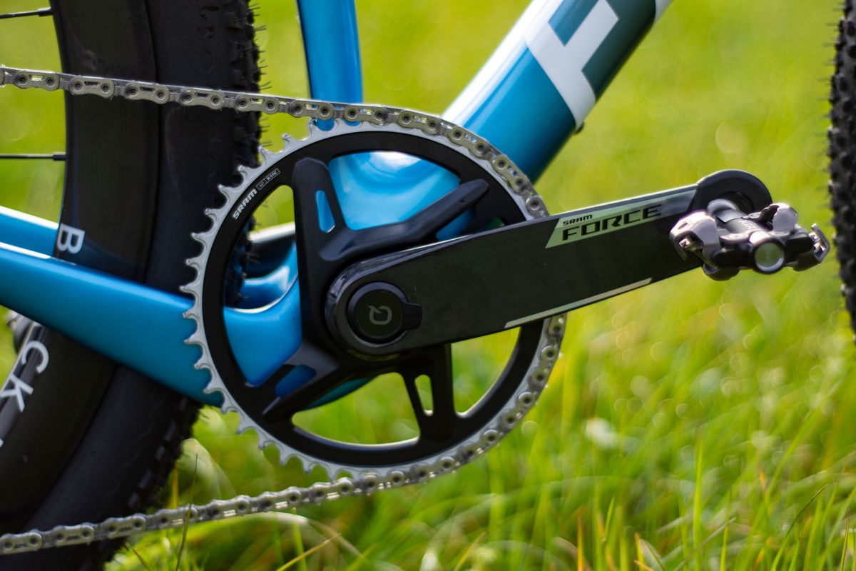 A blue Factor Sarana gravel bike in a grassy field with a hedge in the background