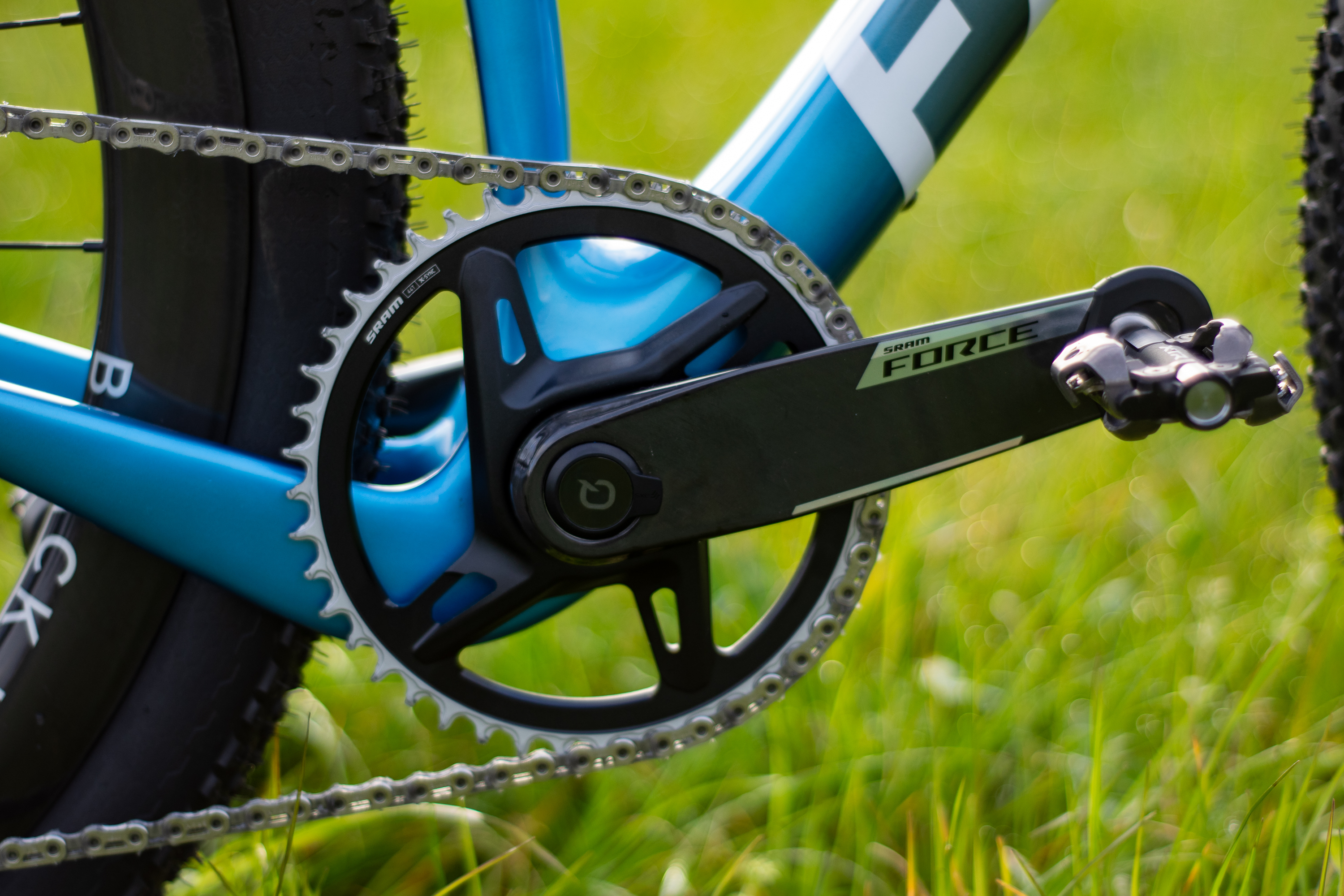 A blue Factor Sarana gravel bike in a grassy field with a hedge in the background