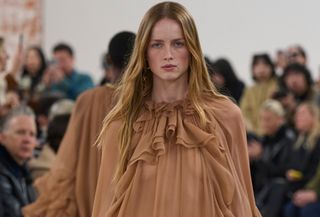 Model Chloe wears a sheer, ruffled dress in bronze at the A/W 24 show.