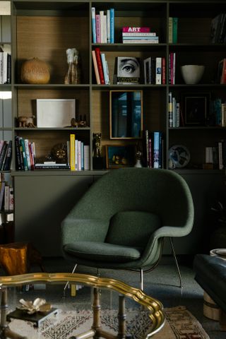 Corner of a study with dark green walls, shelving and armchair