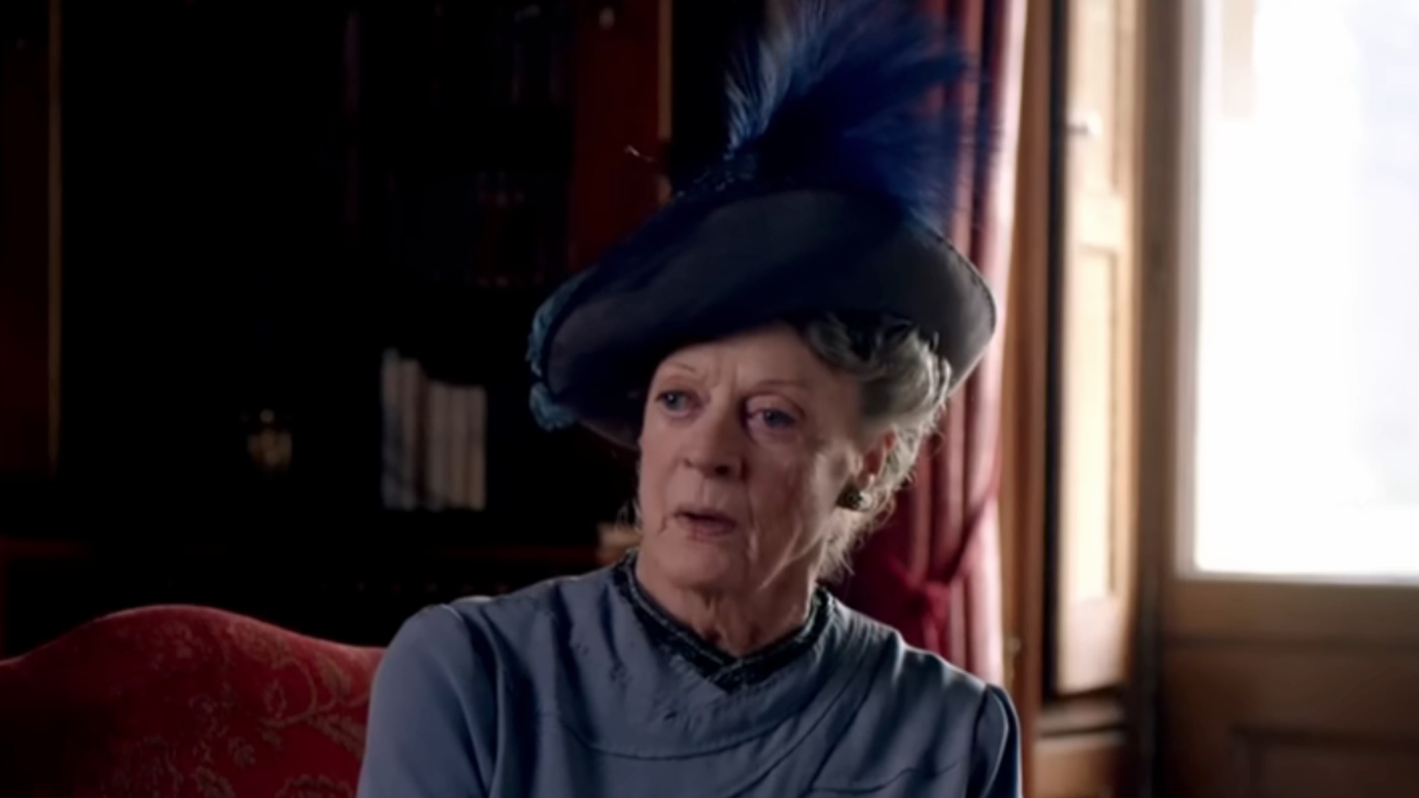 Maggie Smith in a blue dress, and blue hat with e blue feather in Downton Abbey