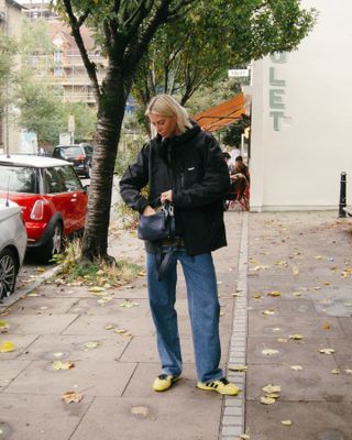 Fashion influencer Lindsey Holland in London wearing a chic fall outfit with jeans, yellow and black Adidas Originals x Wales Bonner SL76 sneakers, and a black Loewe puzzle bag.