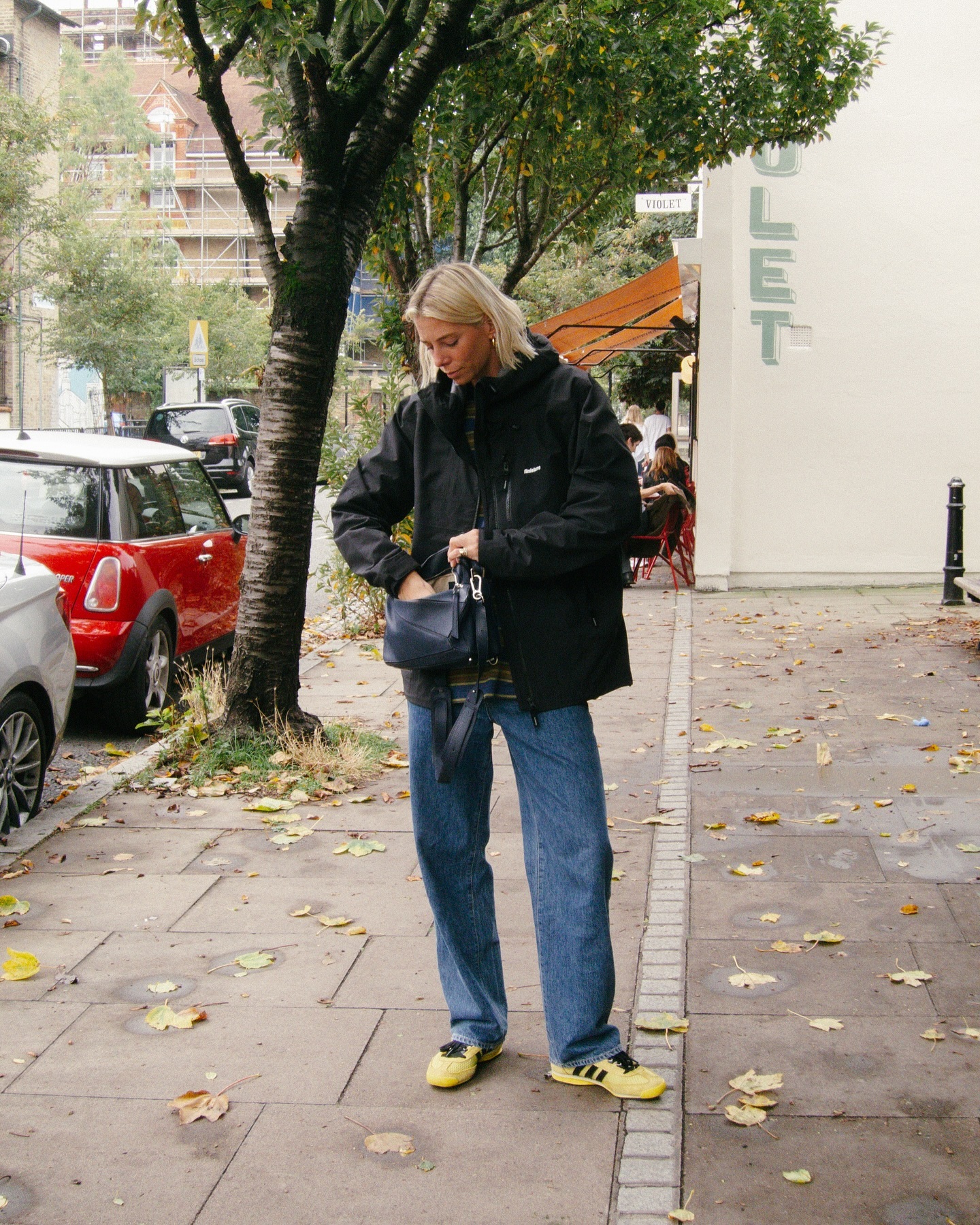 La influencer de moda Lindsey Holland en Londres luciendo un elegante conjunto de otoño con jeans, zapatillas Adidas Originals x Wales Bonner SL76 amarillas y negras y un bolso rompecabezas negro de Loewe.