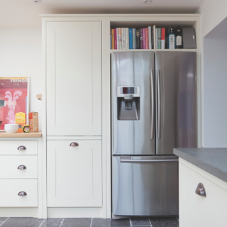 White kitchen units, black floor tiles, large fridge freezer.