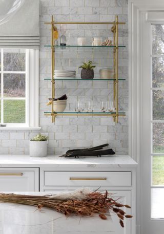 White kitchen with glass and brass shelving unit displaying trinkets and dinnerware