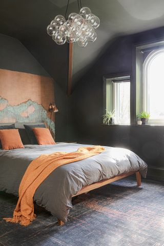 Black bedroom with grey and orange bed linen, copper headboard panel, bubble chandelier