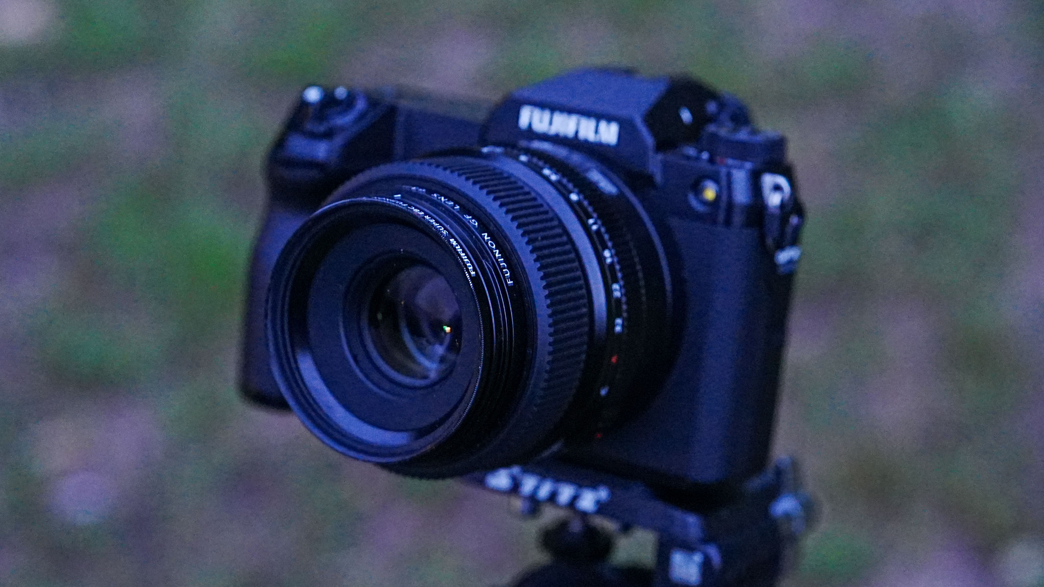 The Fujifilm GFX100S II with the Fujifilm GF 63mm f/2.8 R WR lens attached on a tripod with grass in the background.
