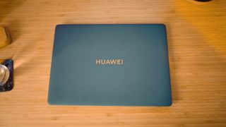 A blue Huawei Matebook X Pro laptop on a wooden desk, in front of blue and orange LED lights.