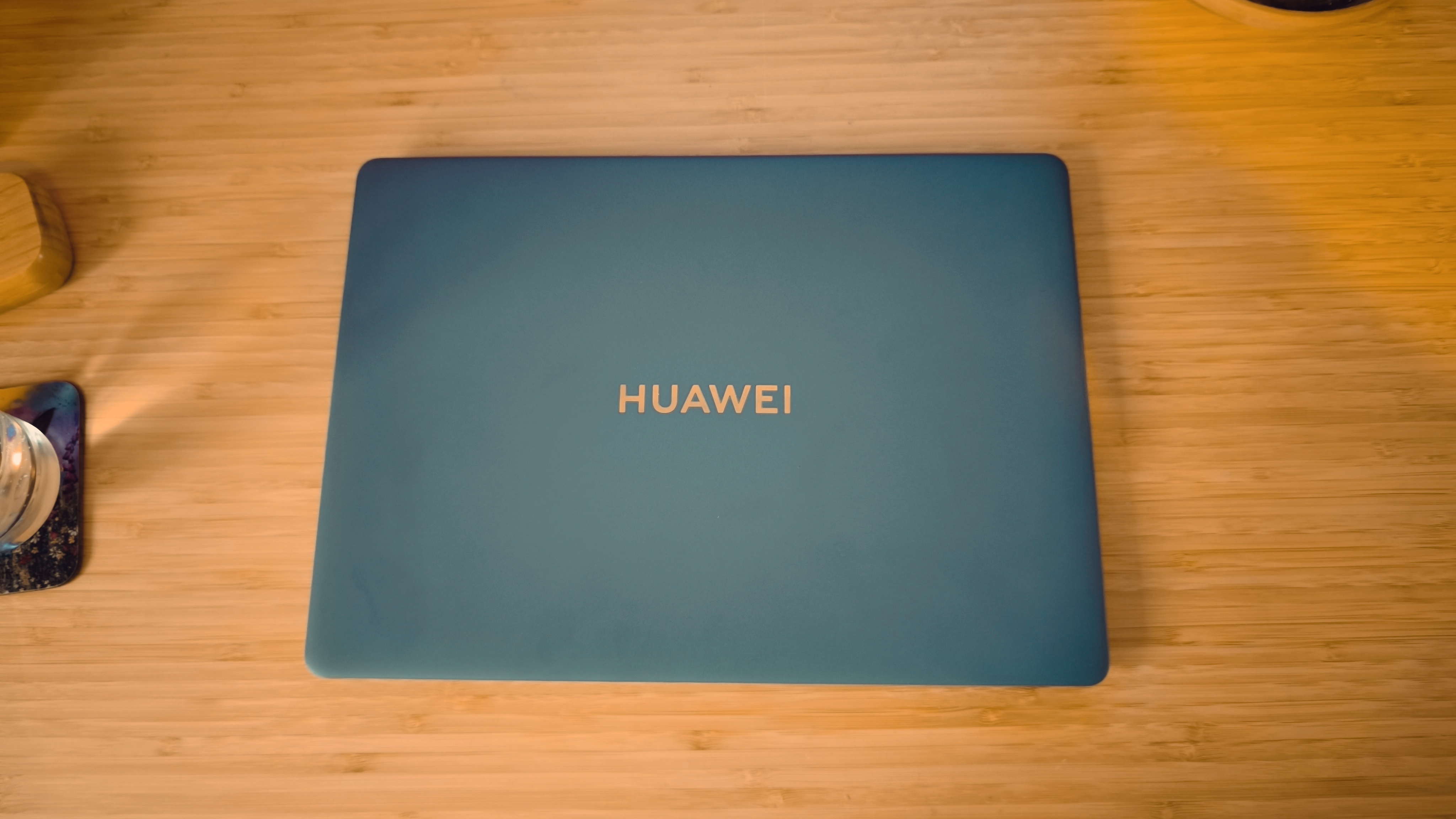 A blue Huawei Matebook X Pro laptop on a wooden desk, in front of blue and orange LED lights.