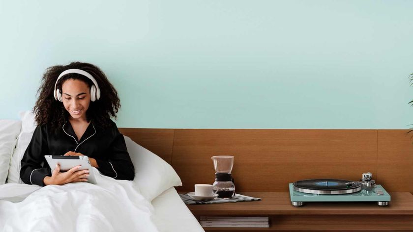 A woman in bed on an iPad and listening to music over headphones, next to a shelf with a coffee drip and TN-400BT-X/TB turntable.