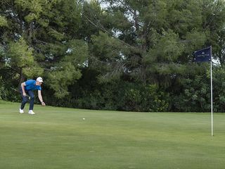 Ben Emerson rolling a golf ball towards the hole to determine the speed of the greens and the putting stroke needed to get the ball close to the hole