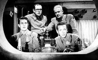 Four men gathers around a vintage spaceship set