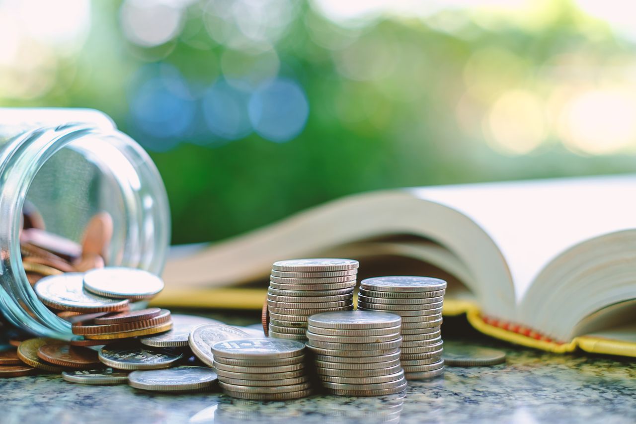 A jar of coins empties next to a book and a pile of stacked quarters